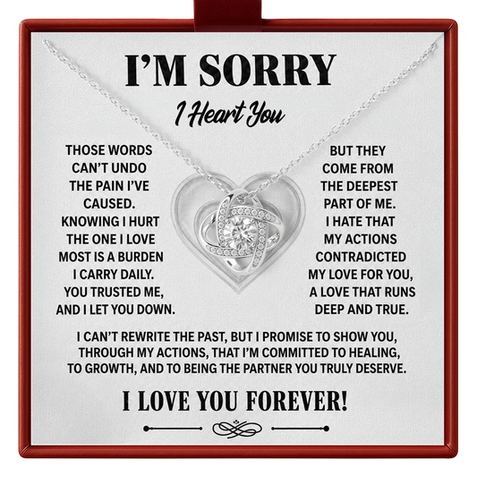 A silver heart-shaped pendant necklace with a central clear rhinestone, presented on a white square card inside a red gift box. The card features black text reading 'I'M SORRY I Heart You' and sentimental apology messages, with the necklace draped across the top.