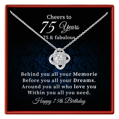A silver 75th birthday necklace with a floral knot pendant displayed on a black presentation card inside a red gift box. The card features elegant white text celebrating a 75th birthday with a sentimental message.