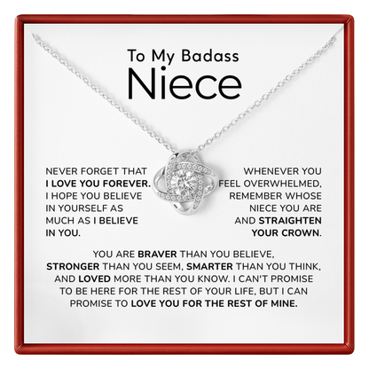 A silver necklace with a heart-shaped pendant set with small clear stones, presented on a white card with a red border. The card is addressed 'To My Badass Niece' and features a sentimental message printed in black text.