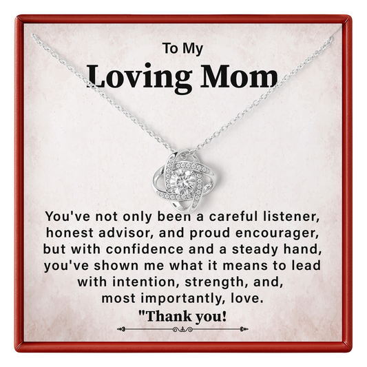 A silver necklace with a heart-shaped pendant displayed on a personalized gift card. The card has a red border and a warm beige background with a sentimental message addressed to 'Loving Mom'.