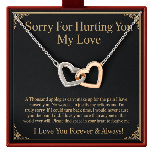 A necklace with two interlocking heart pendants, one silver and one rose gold, presented on a black gift card inside a red box. The card features a sentimental message for a broken heart.