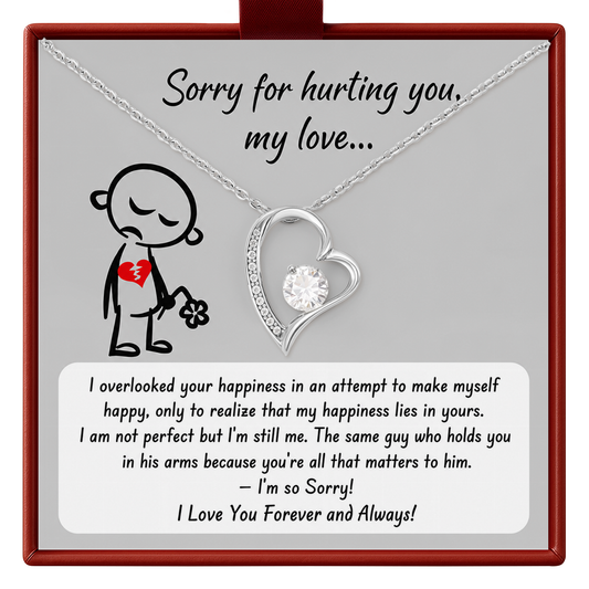 A silver heart necklace with a clear rhinestone pendant is displayed on a gray gift card inside a red box. The card features a black line drawing of a broken heart and a heartfelt apology message.