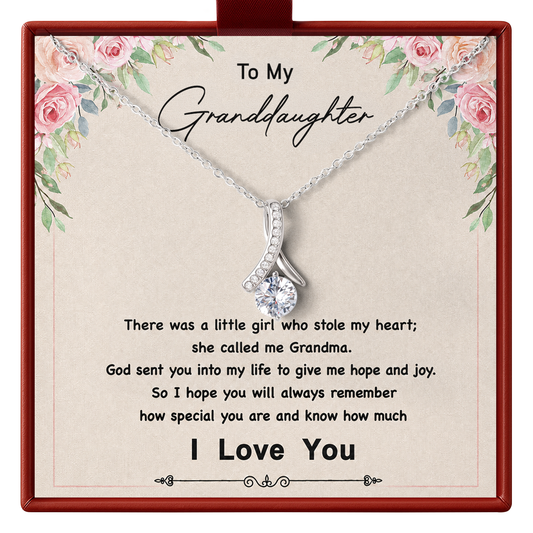 A silver necklace with a clear rhinestone pendant displayed on a printed gift card addressed 'To My Granddaughter,' inside a red gift box.