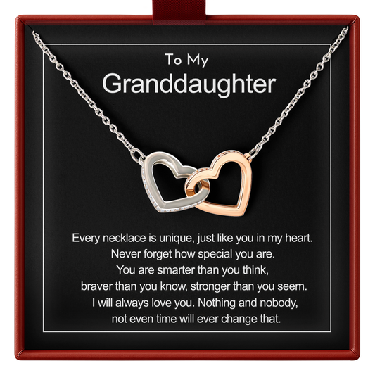 A heart-shaped pendant necklace with one silver heart and one rose gold heart interlocking, presented on a black gift card inside a red square box. The card is personalized with the text 'To My Granddaughter' and a sentimental message.