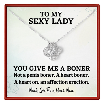 Necklace with heart pendant on a card with humorous text, displayed in a red border.