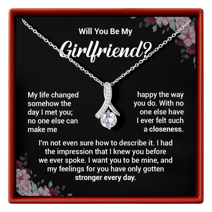 Necklace with a diamond pendant in a box with romantic message, surrounded by floral decorations.