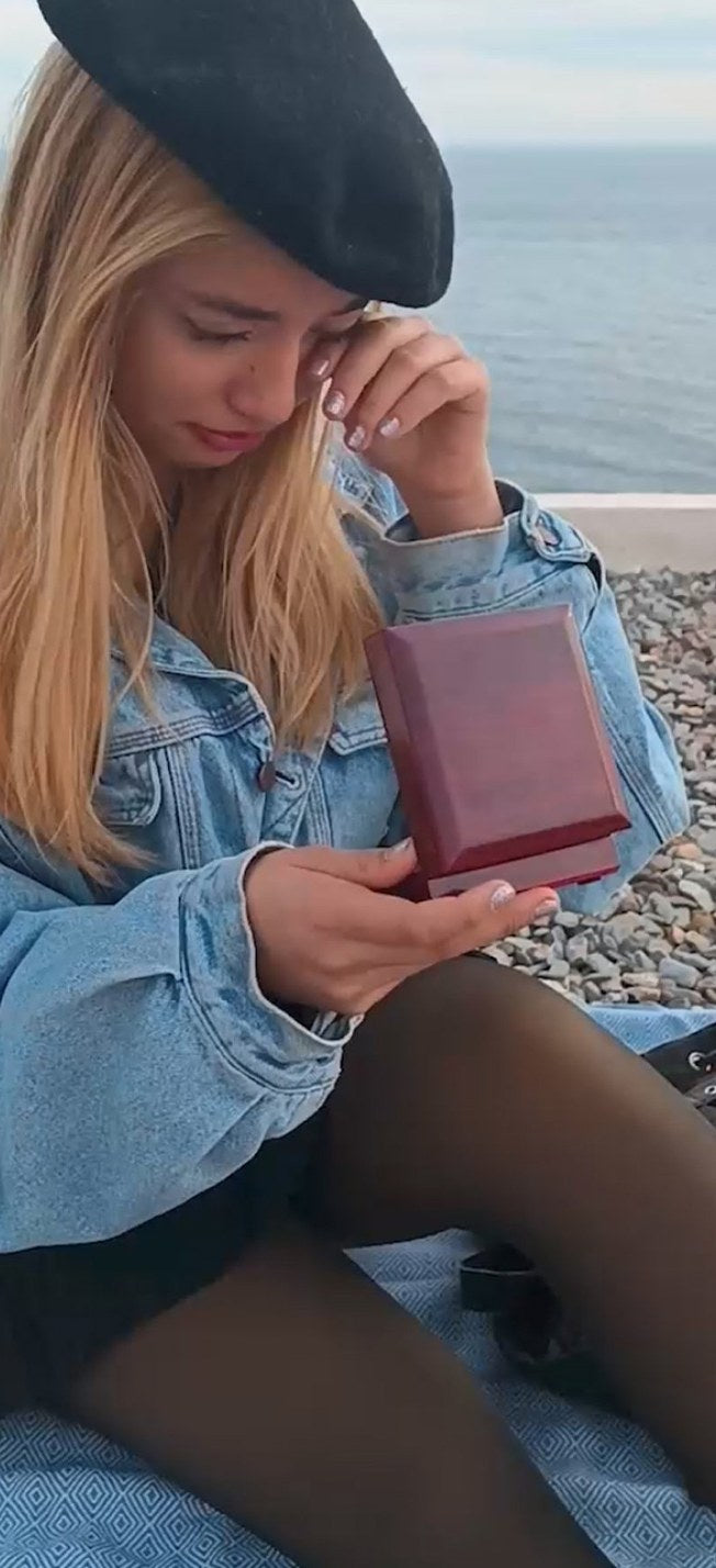 Woman moved to tears holding a JeweLayer necklace gift box by the sea